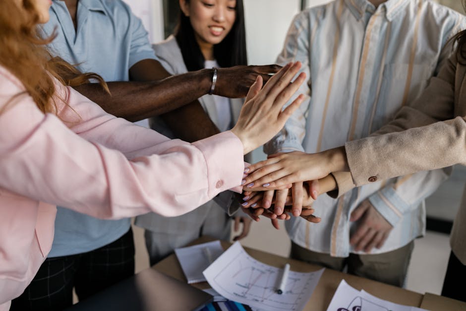 Diverse team members putting hands together in an office, symbolizing collaboration and unity