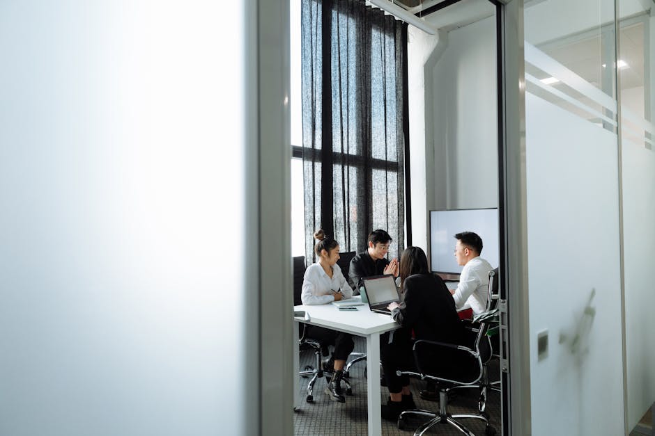 Group collaborating in a well-lit office room with large windows, discussing business strategies.