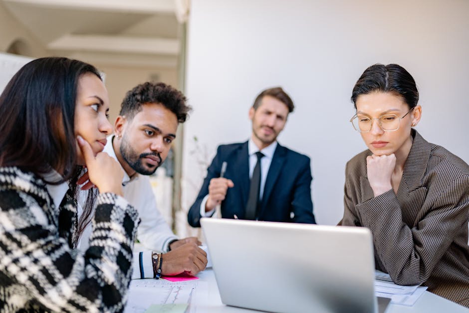 A diverse group of professionals working together around a laptop in a modern office setting