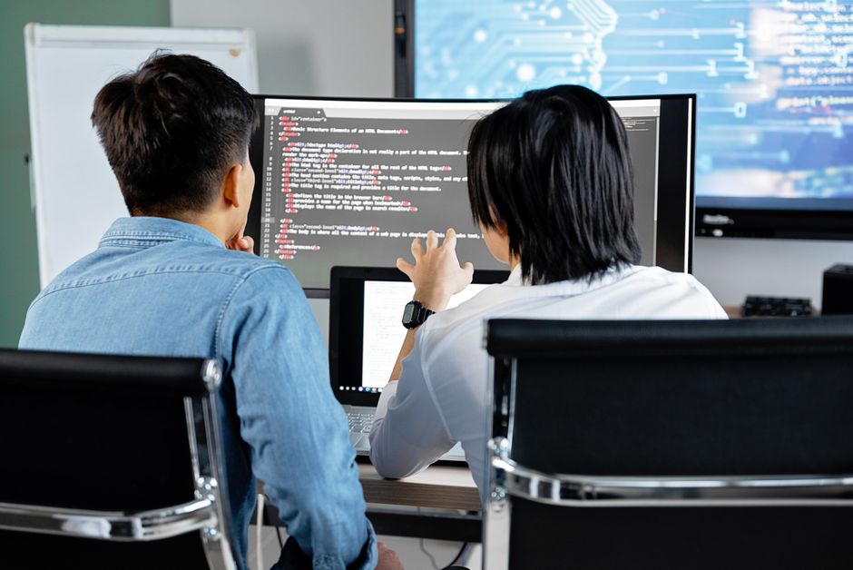 Two developers working together discussing code on a screen.
