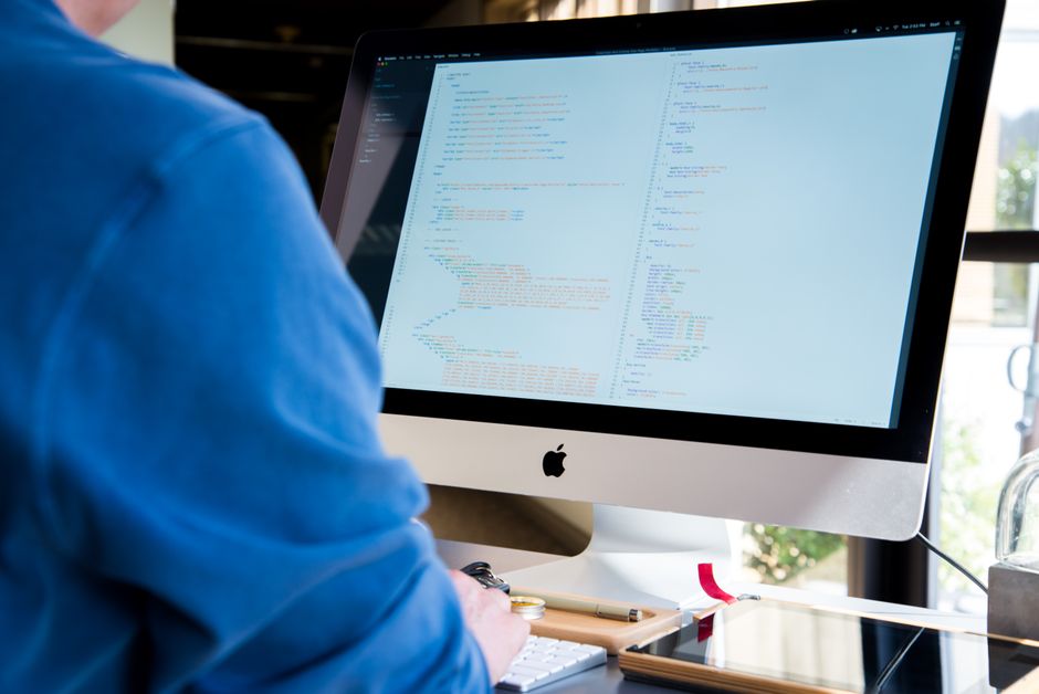A programmer in a blue shirt coding on an iMac.