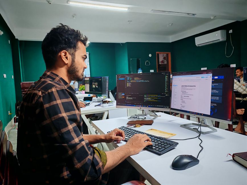 Software developer working on code at a dual monitor setup in a modern office.