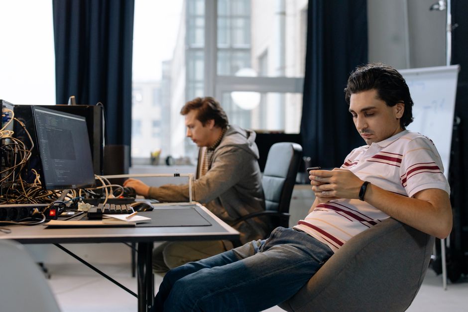 Dvojica muškaraca rade u modernom uredu, jedan na računalu, drugi na pametnom telefonu